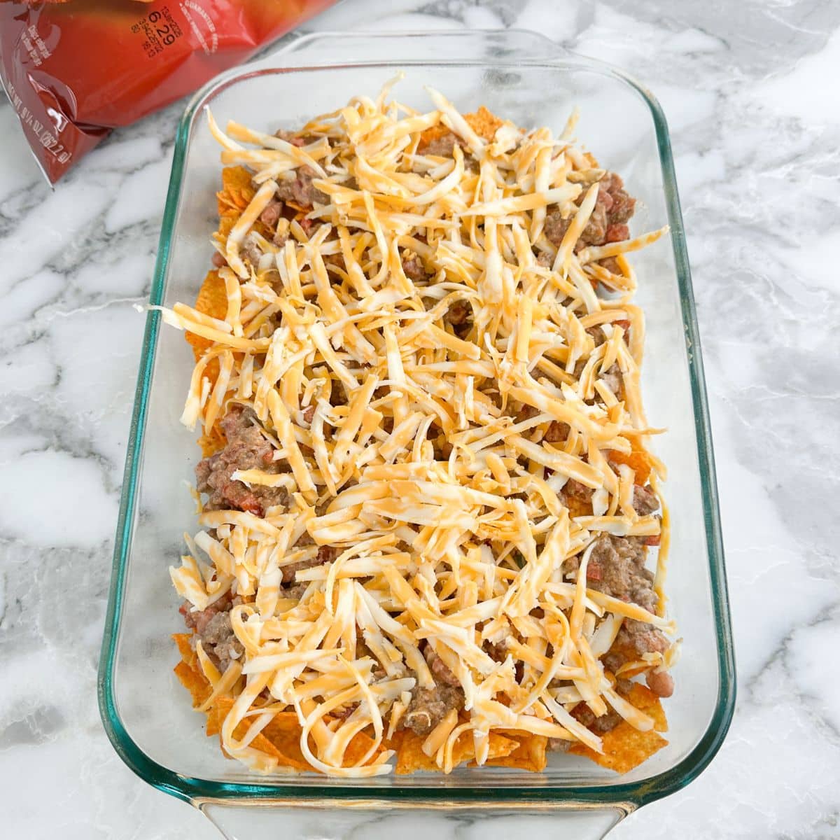 Casserole dish with Doritos chips with ground beef and shredded cheese.