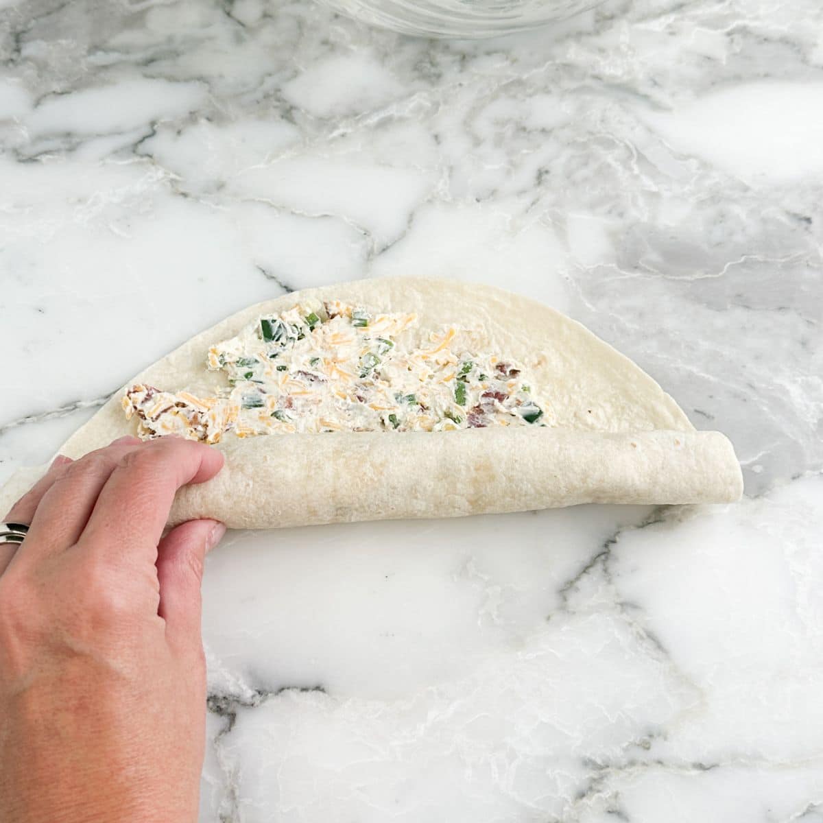 Hand rolling up tortilla pinwheel.