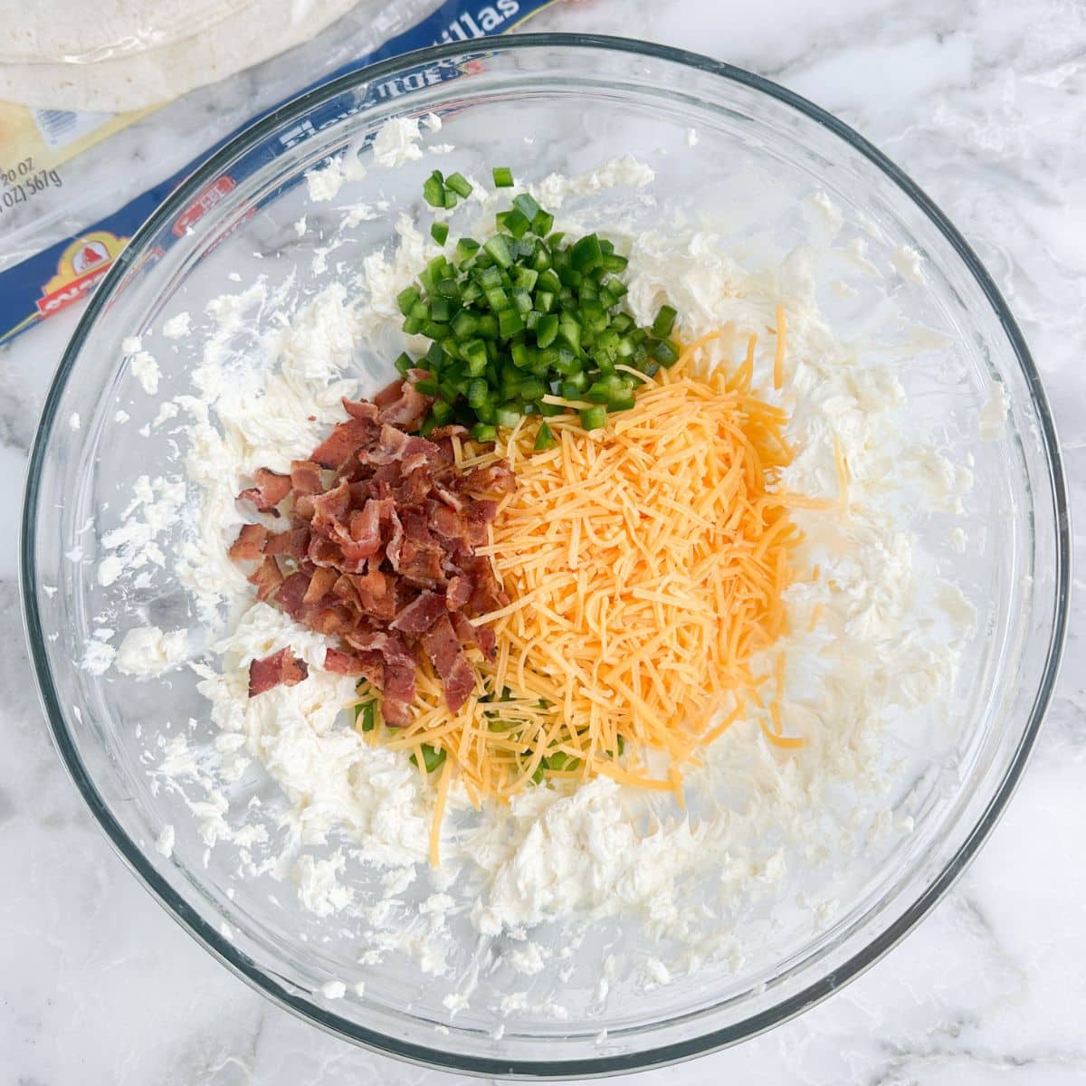 Bowl of creamy cream cheese, shredded cheese, crumbled bacon, and jalapenos.