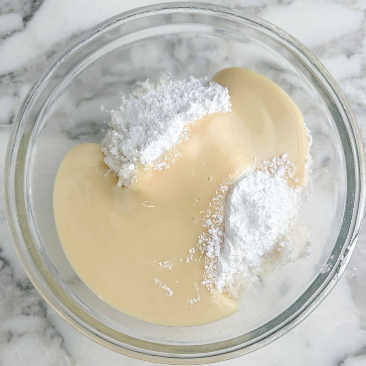 Bowl with sweetened condensed milk, powdered sugar, and shredded coconut. 