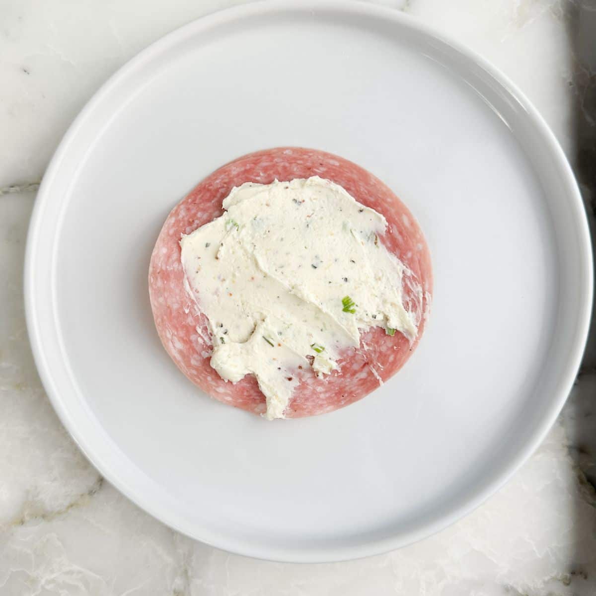 Piece of salami spread with cream cheese.