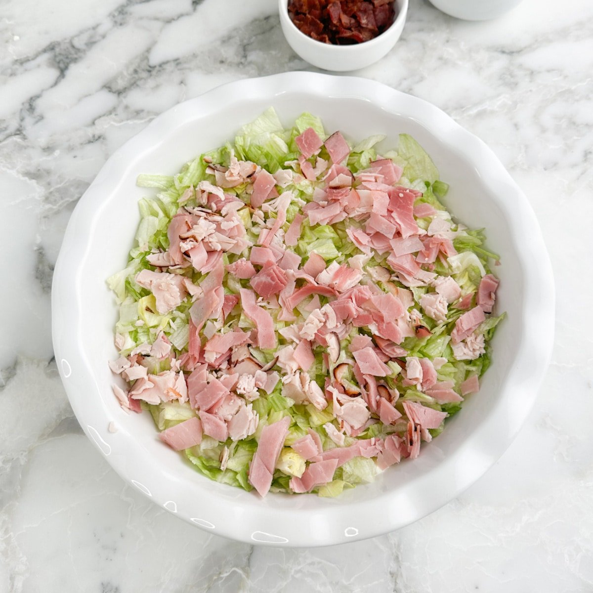 Serving dish with cream cheese, chopped lettuce, and chopped turkey and ham.