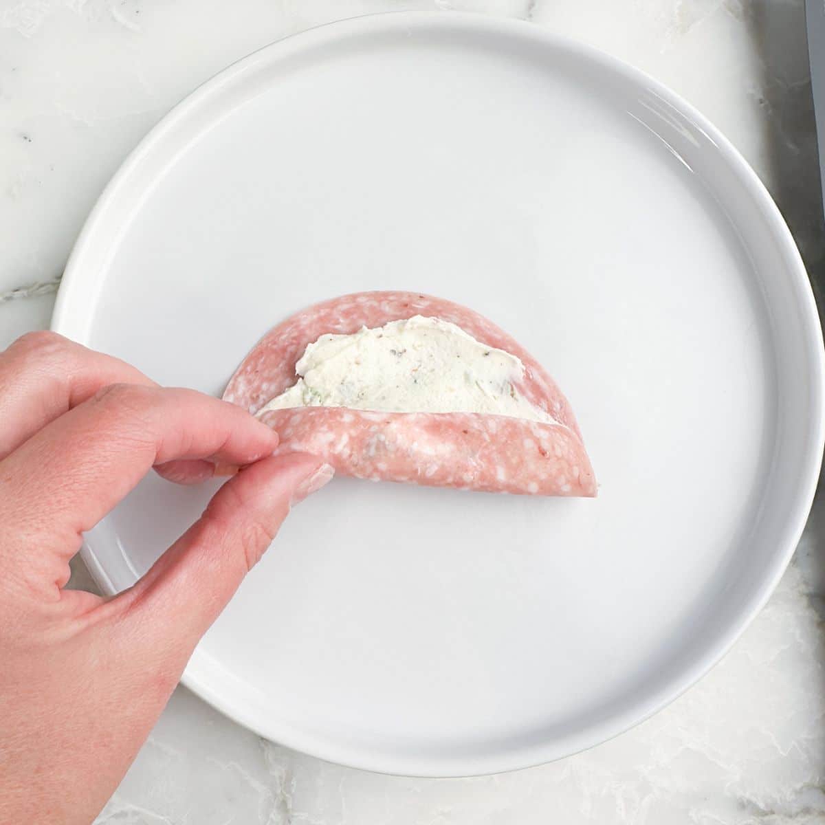 Piece of salami with cream cheese being rolled up.