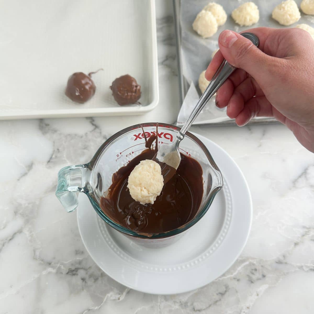 Coconut ball dipping into melted chocolate.