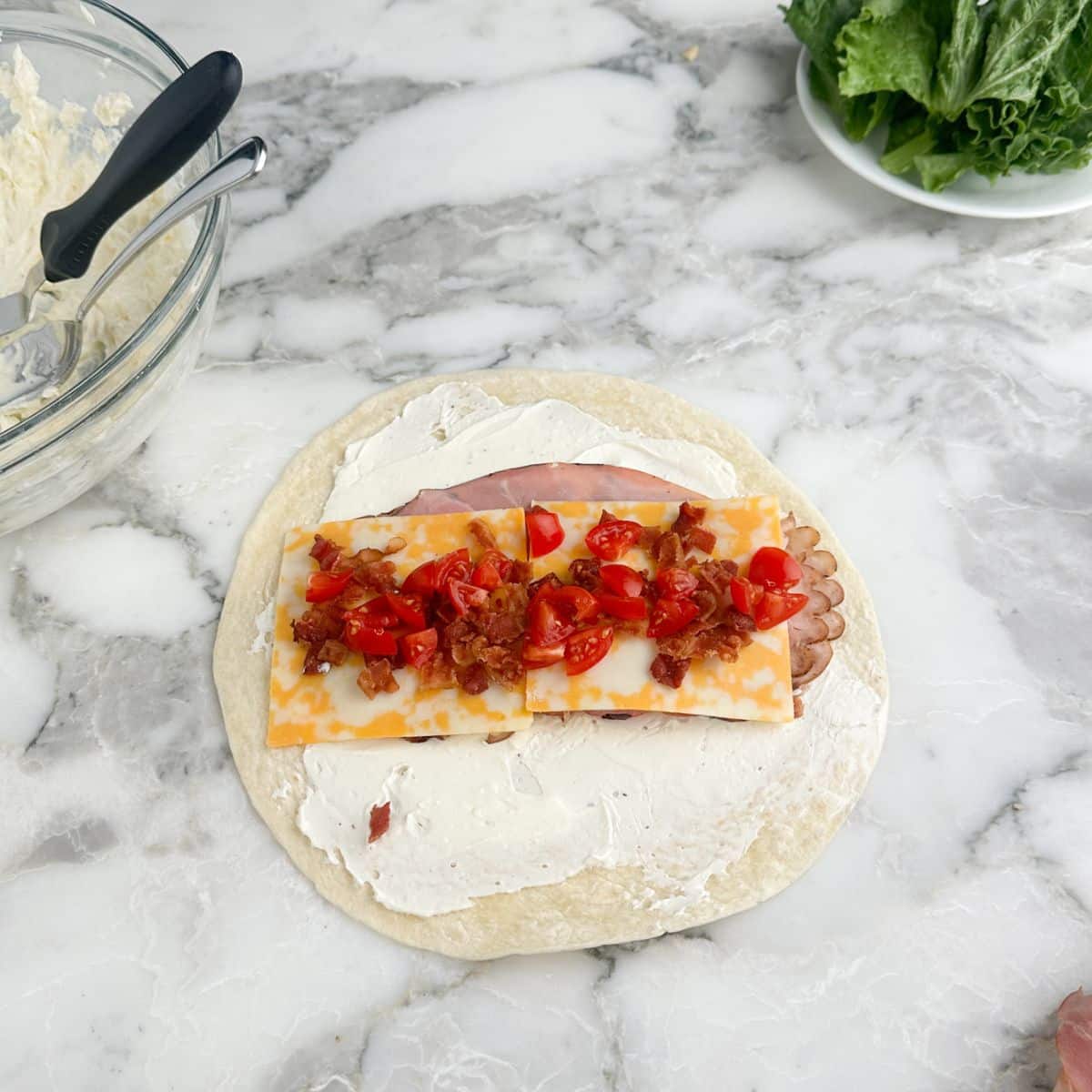 Tortilla topped with cream cheese, ham, cheese, bacon, and diced tomatoes.