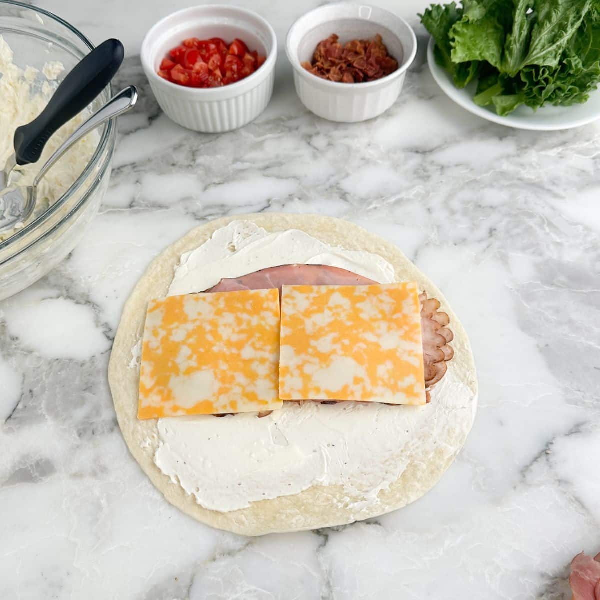 Tortilla topped with cream cheese, turkey, ham, and sliced cheese.