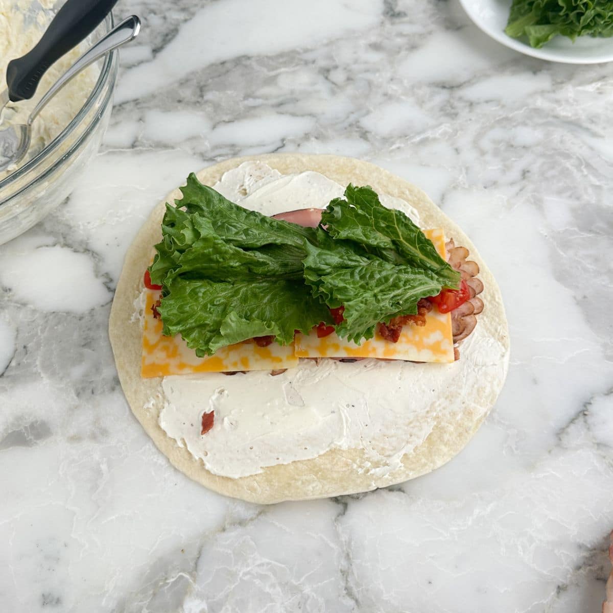 Tortilla topped with cream cheese, ham, cheese, tomatoes, and lettuce.