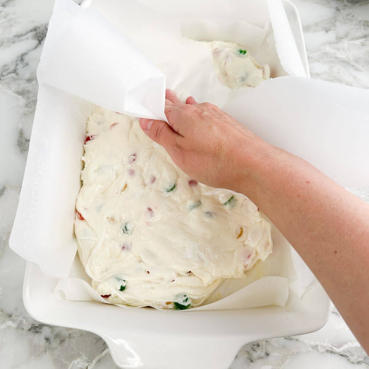 Hand pressing down nougat candy with parchment paper. 