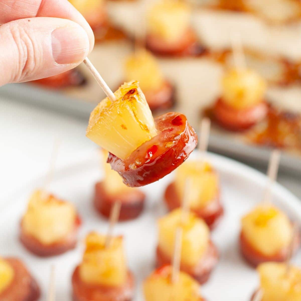 Hand holding a pineapple kielbasa bite.