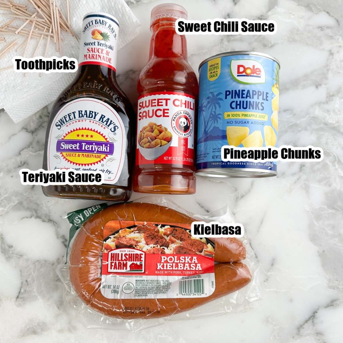 Bottle of teriyaki sauce, sweet chili sauce, can of pineapple chunks, and kielbasa.