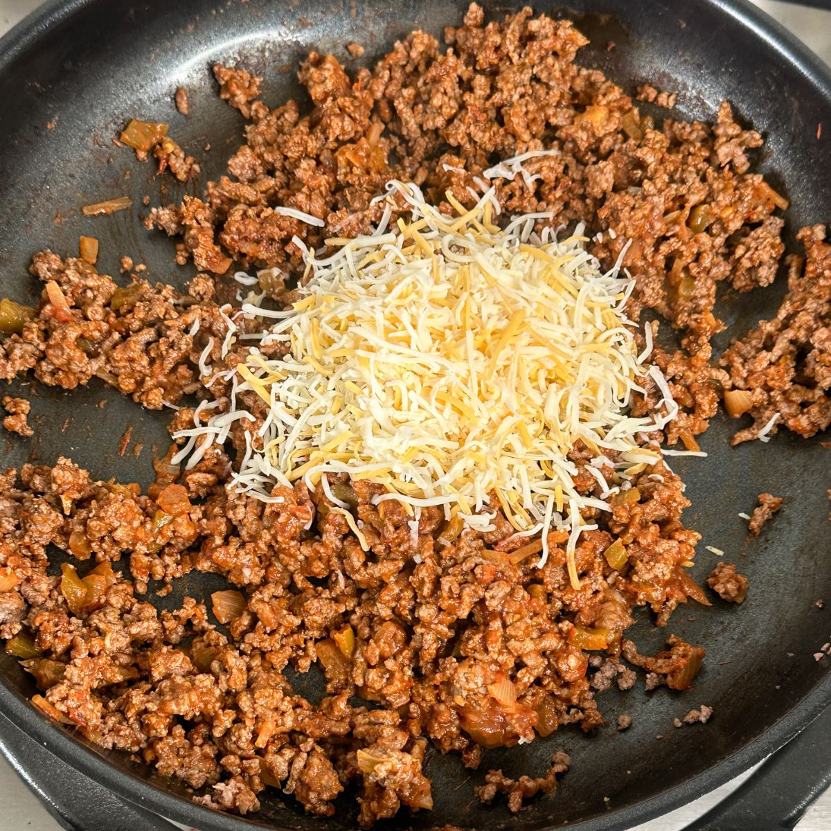 Skillet with seasoned ground beef and shredded cheese.