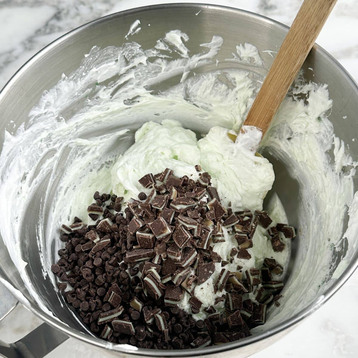 Mixing bowl with cream cheese, mini chocolate chips, and chopped Andes mints.