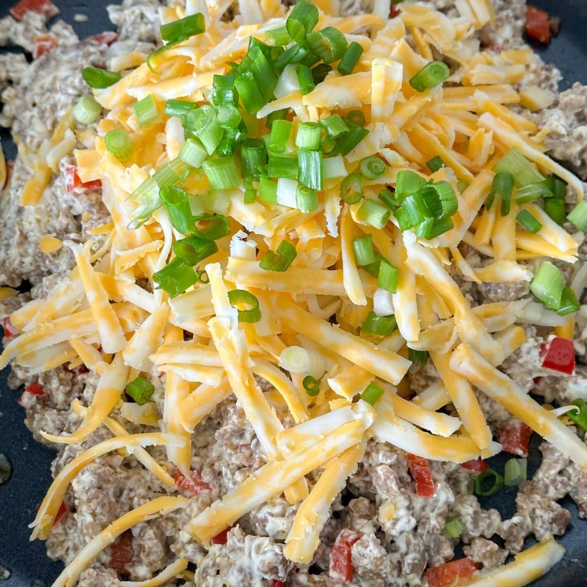 Skillet with ground sausage, shredded cheese, and green onions.