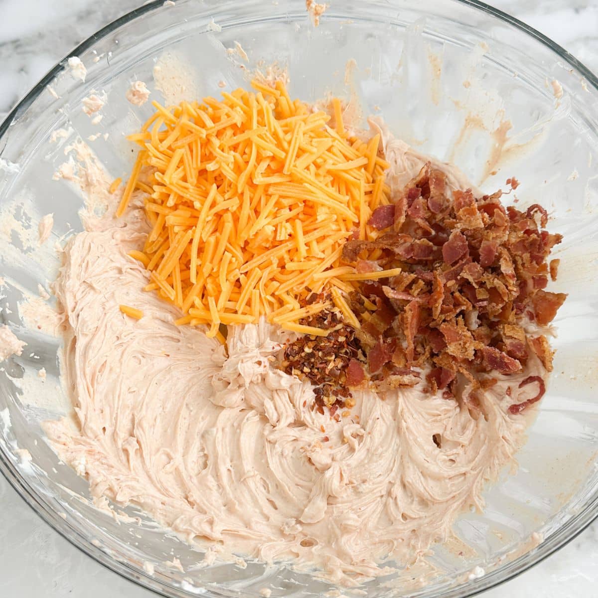 Bowl of seasoned cream cheese, shredded cheese, and crumbled bacon.