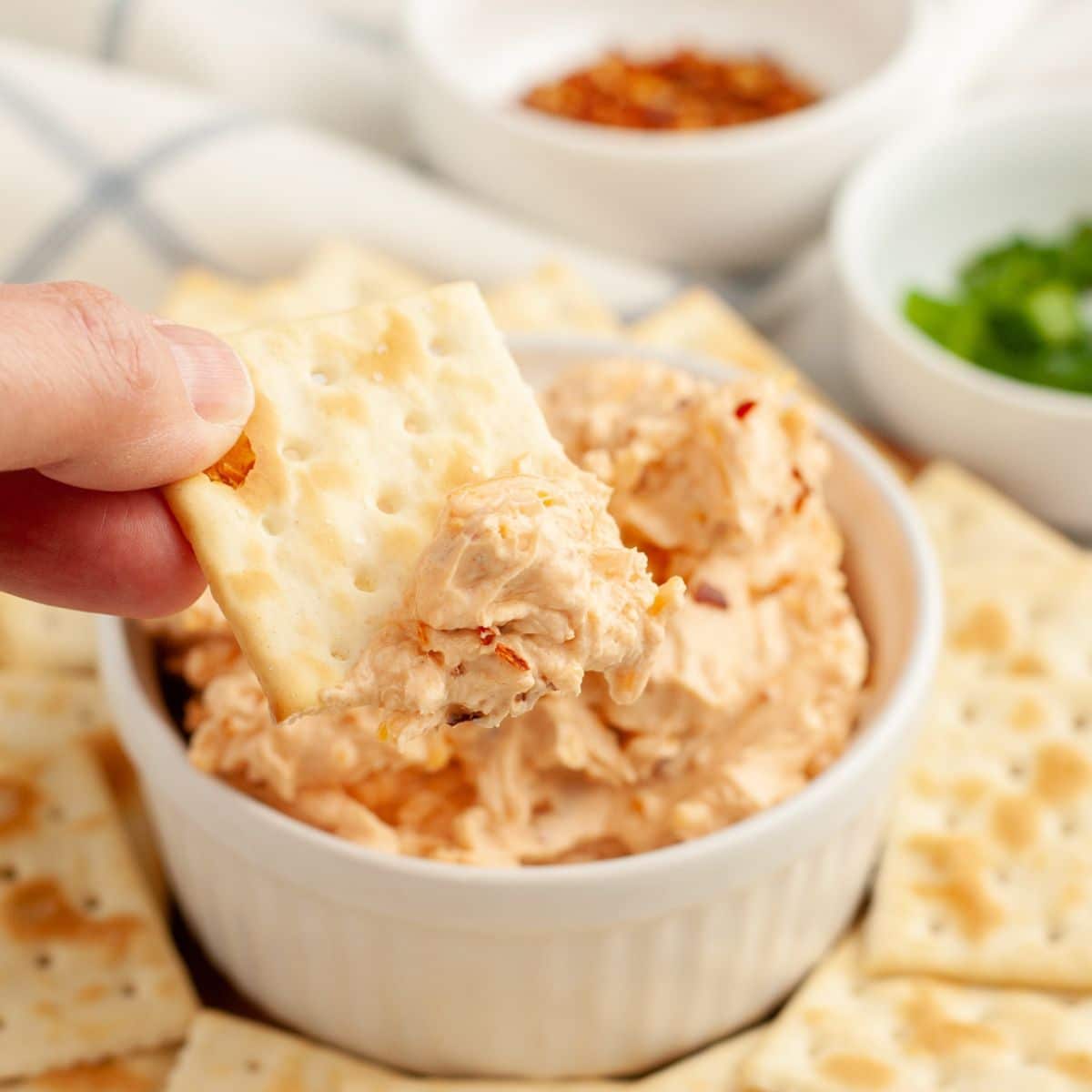 Bowl of fire cracker dip with a hand holding a cracker. 