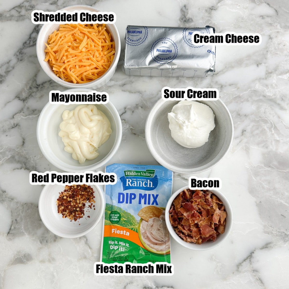 Pack of Fiesta Ranch seasoning, bowls of shredded cheese, mayonnaise, sour cream, cream cheese, crumbled bacon, and red pepper flakes. 