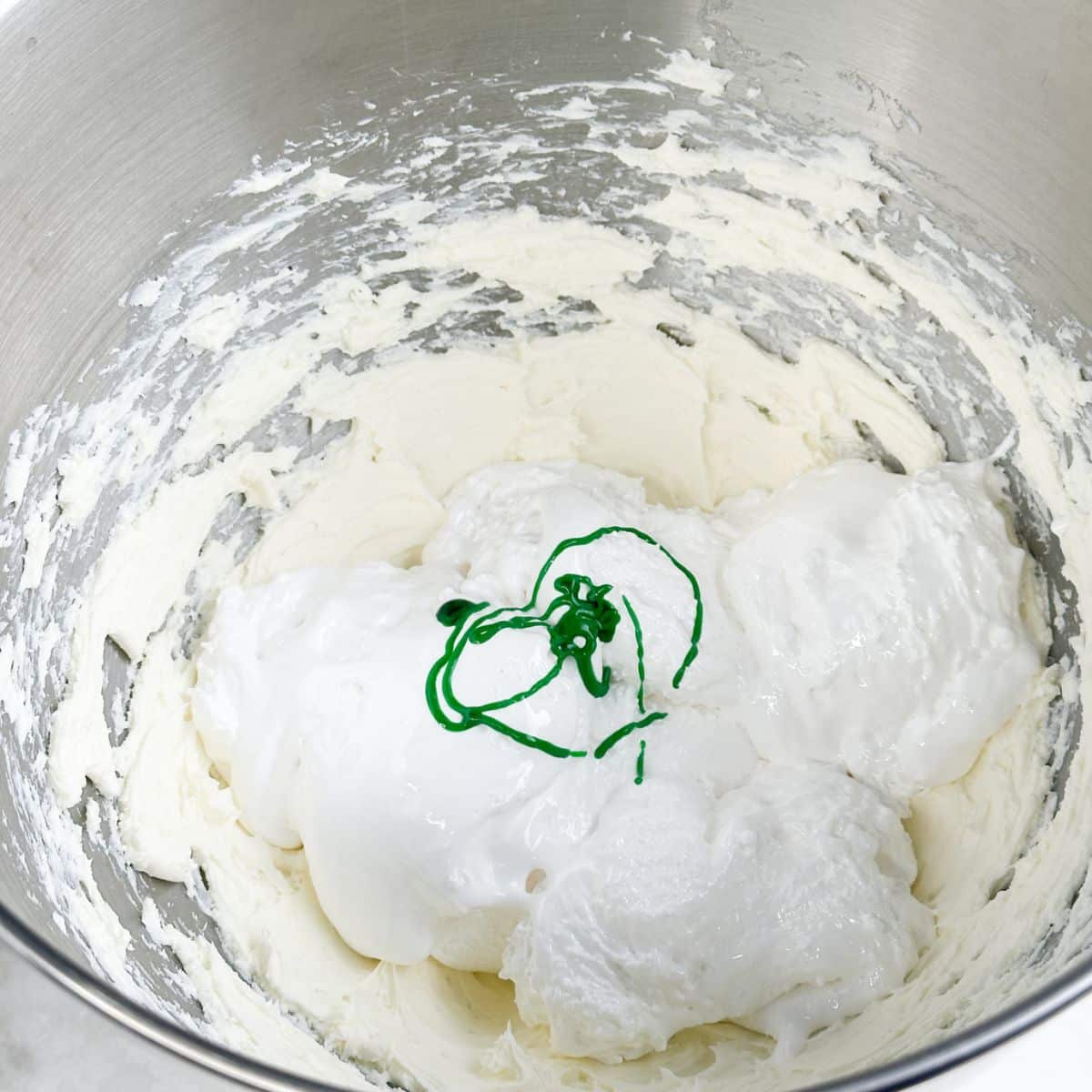 Mixing bowl with cream cheese, marshmallow creme, and green food coloring.
