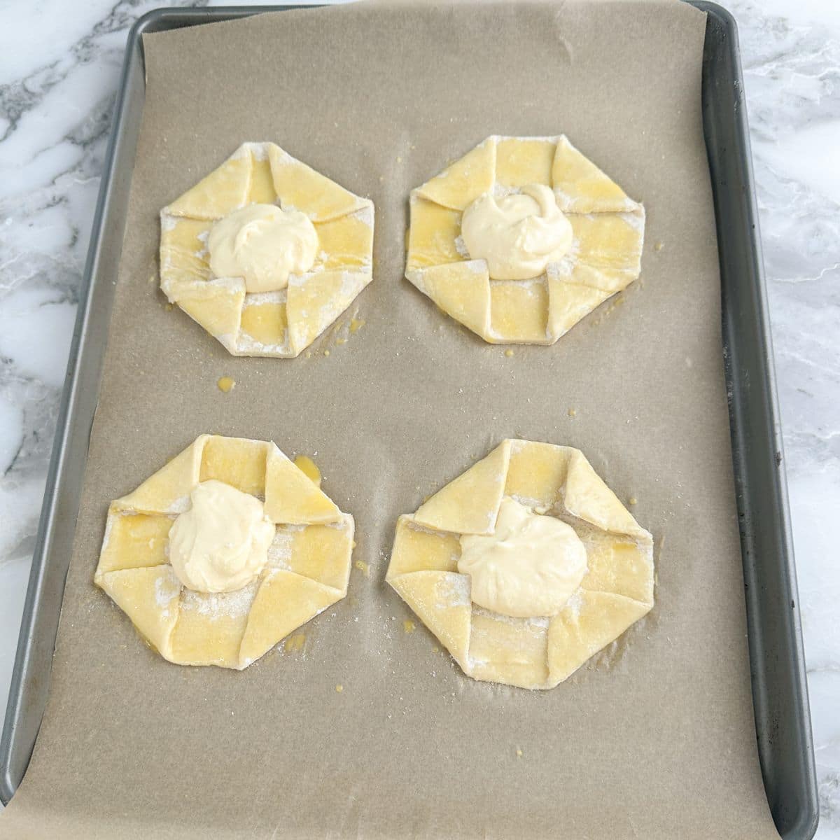 Baking sheet with uncooked cream cheese danish.