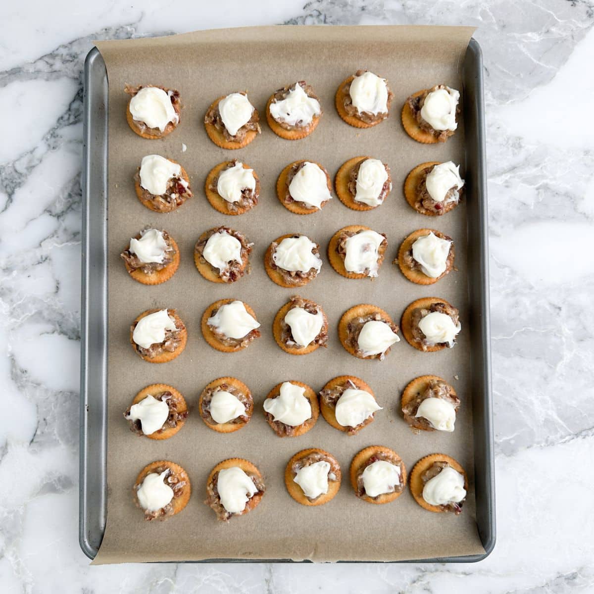 Baking pan with Ritz crackers topped with pecans and frosting. 