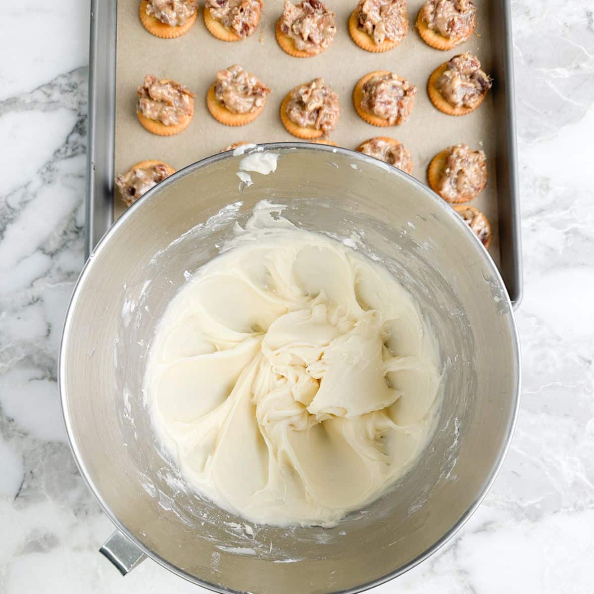 Bowl of cream cheese frosting and pan or Ritz cookies. 