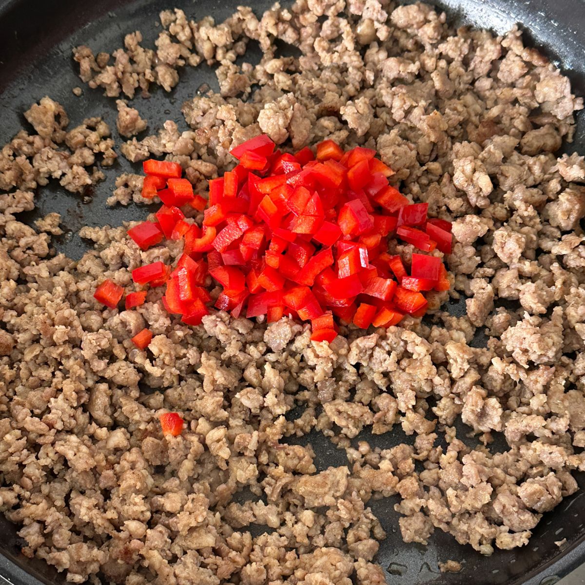 Skillet with cooked ground sausage and red pepper.