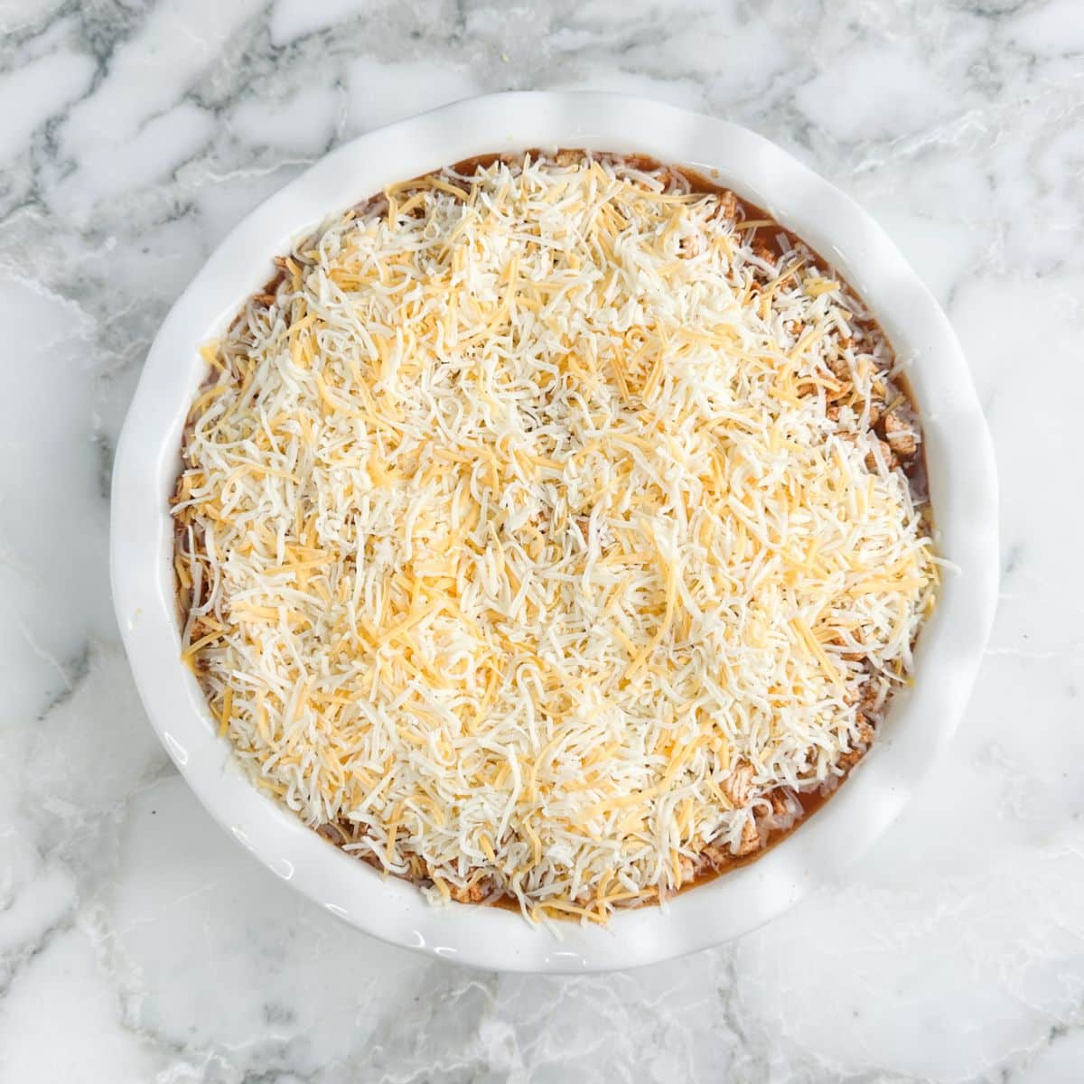 Pie dish with chicken topped with shredded cheese.