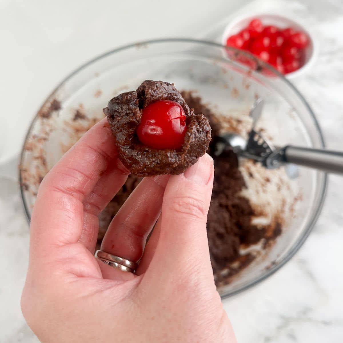 Hand holding brownie bite batter with a cherry in the center. 