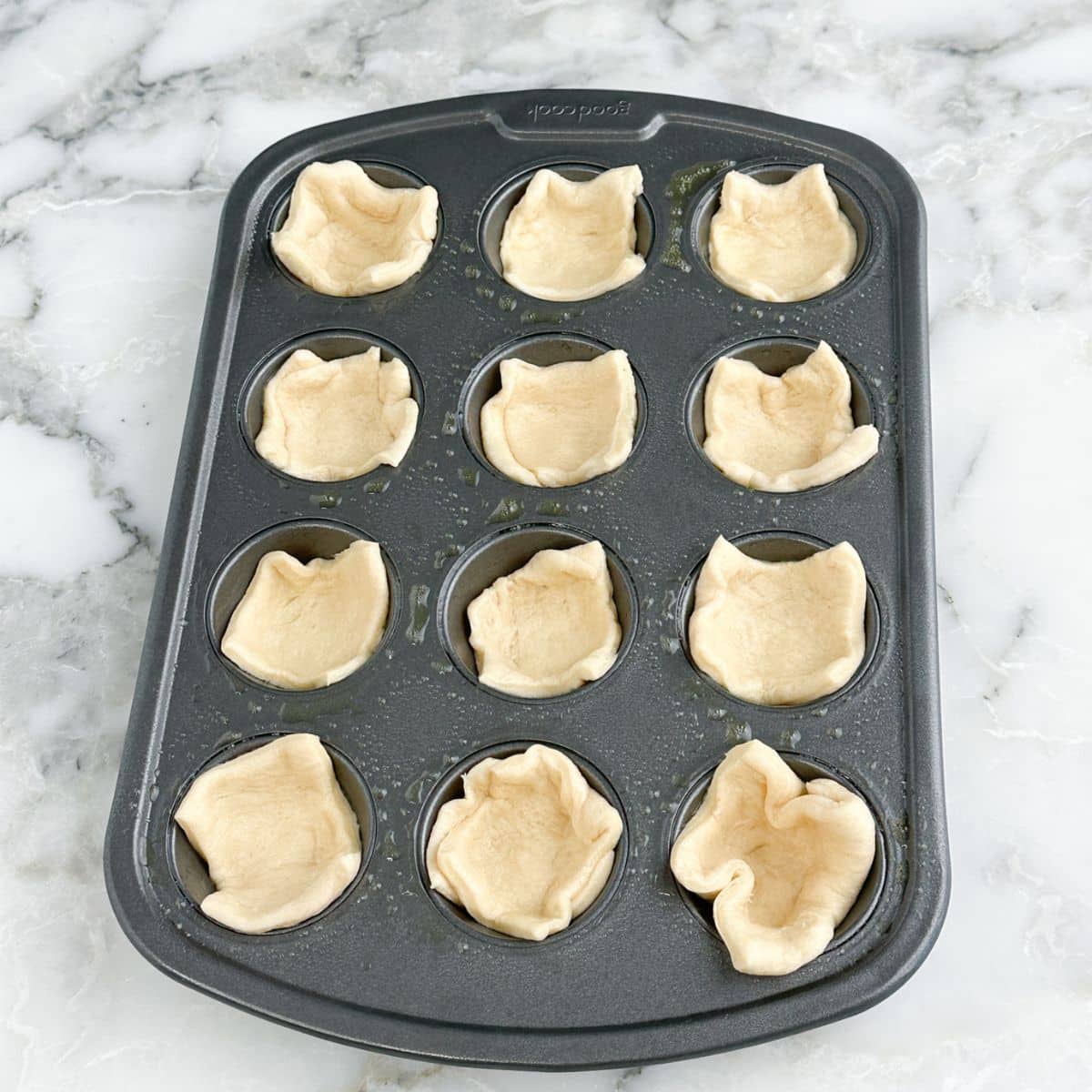 Mini muffin tin with crescent roll dough in the cups. 