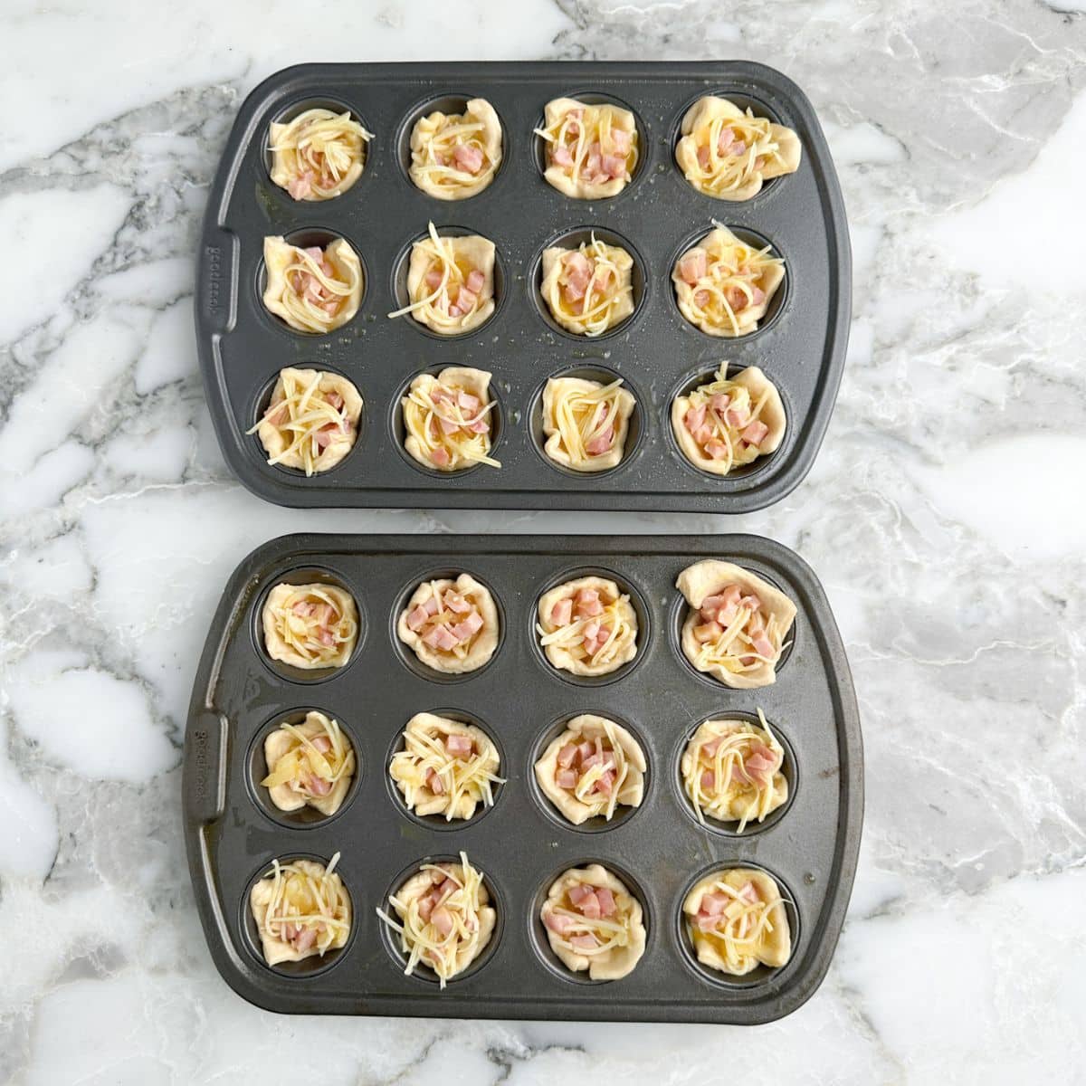 Mini muffin tins with uncooked ham puffs. 