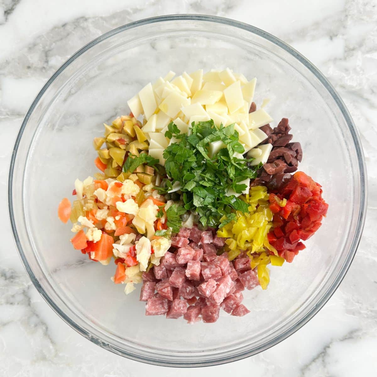 Bowl of diced salami, cheese, parsley, olives, and peppers.