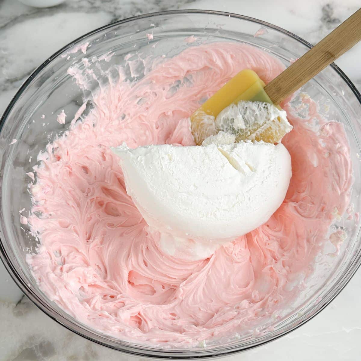 Bowl of pink cream cheese and Cool Whip with a spatula. 