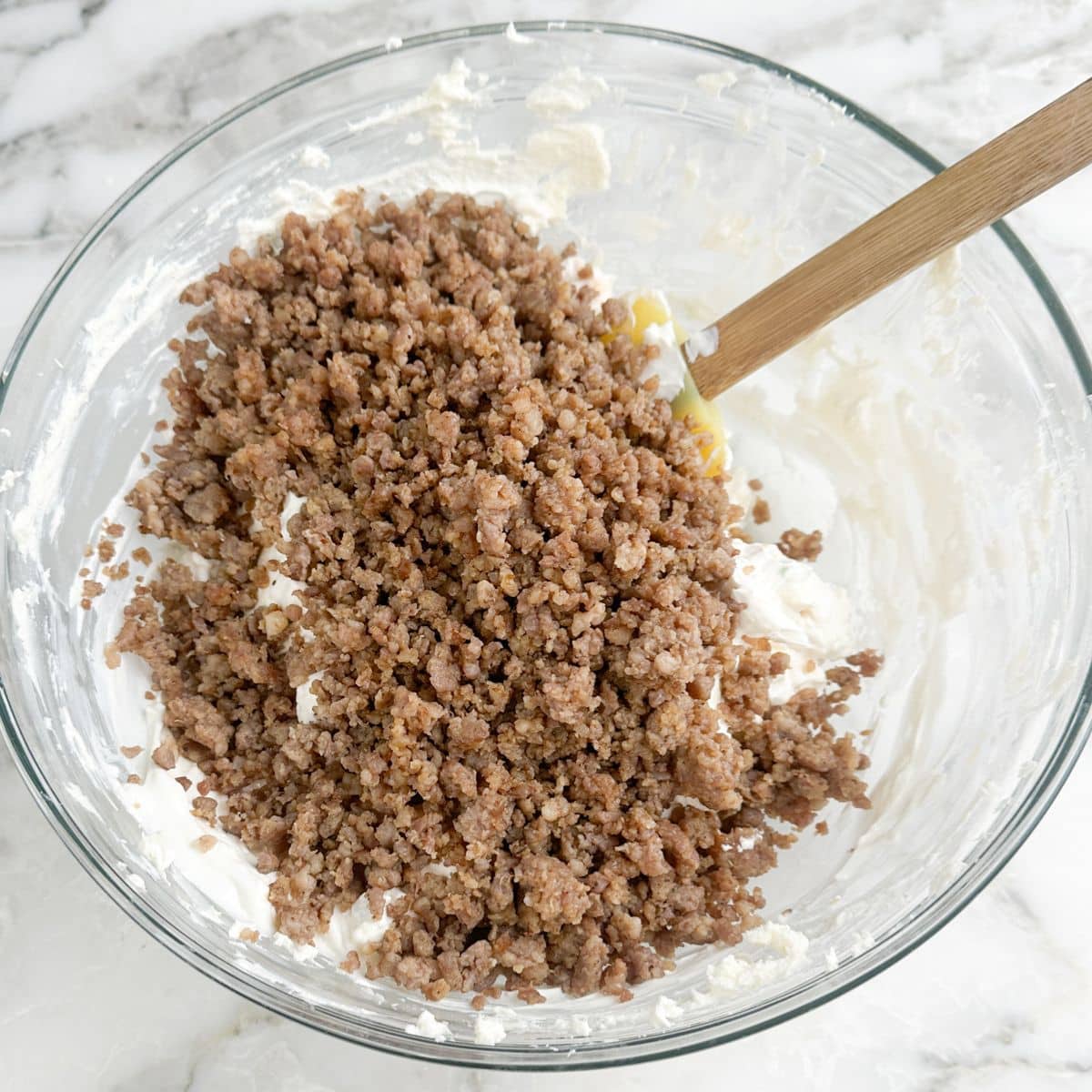 Bowl with cream cheese and cooked, crumbled sausage.
