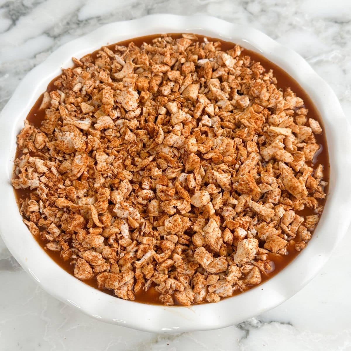 Pie dish with seasoned shredded chicken.