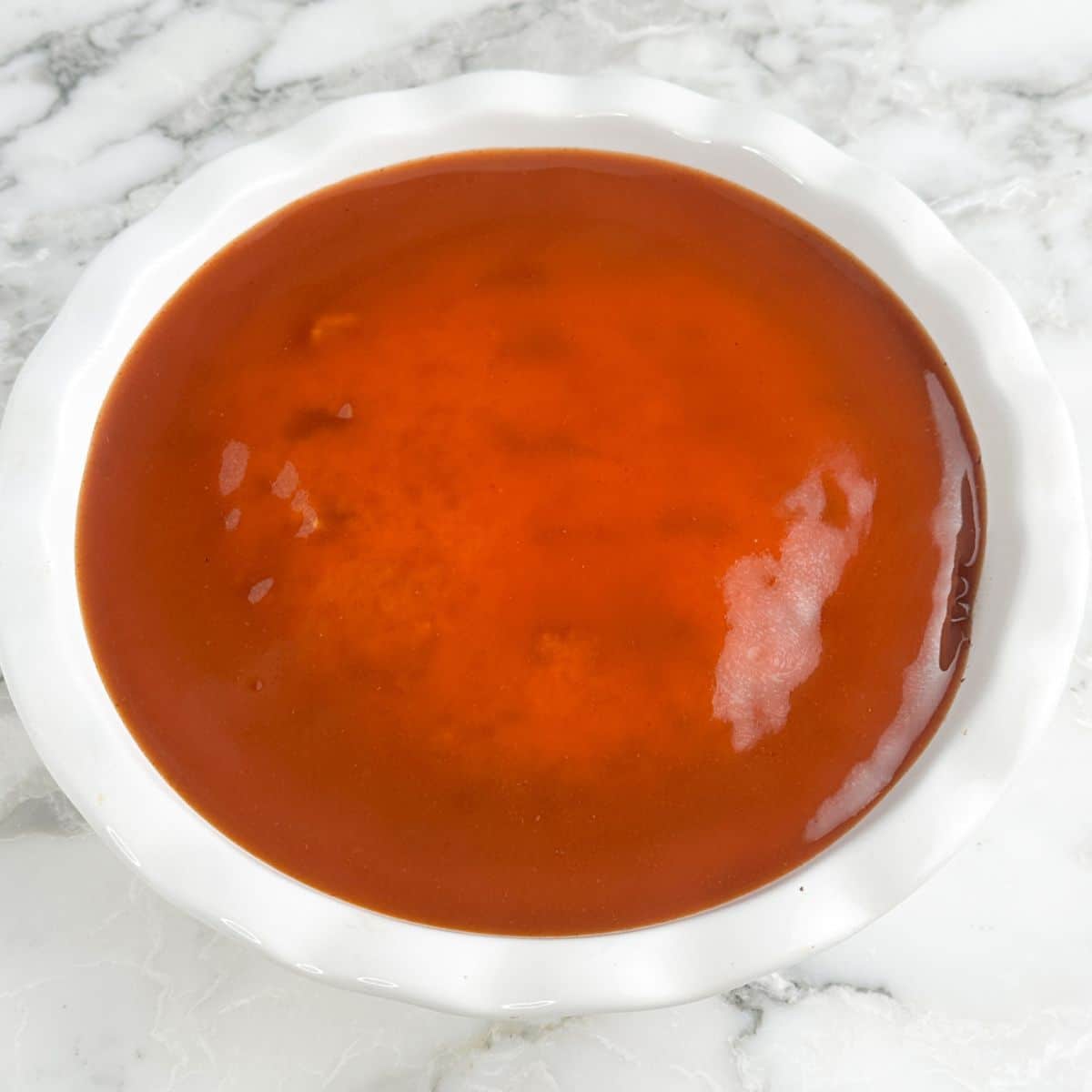 Pie dish with cornbread topped with enchilada sauce.