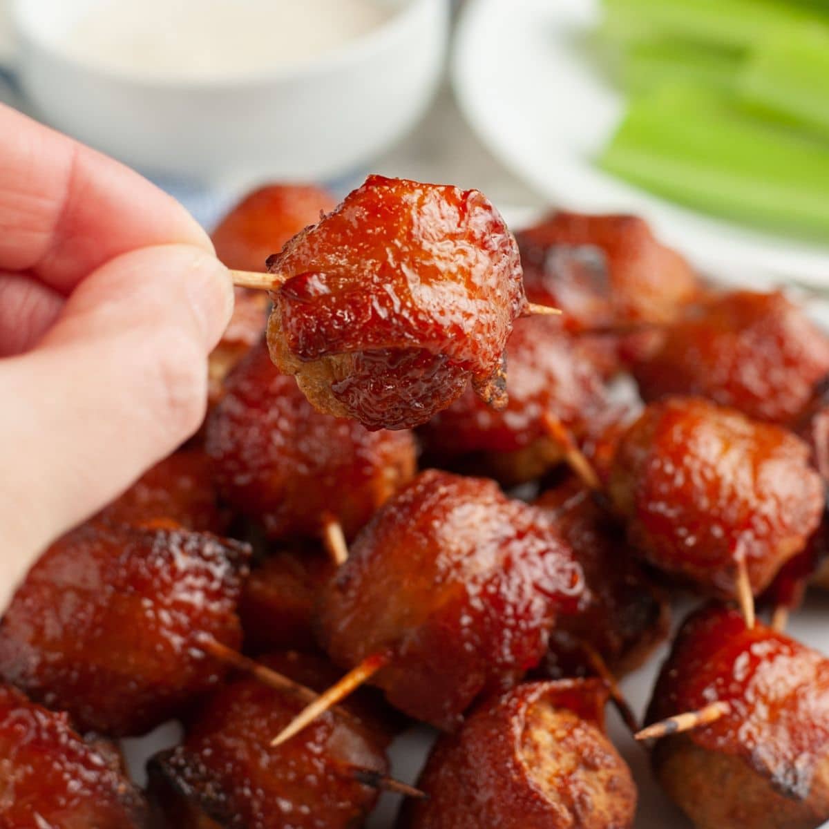Hand holding a bacon wrapped meatball.
