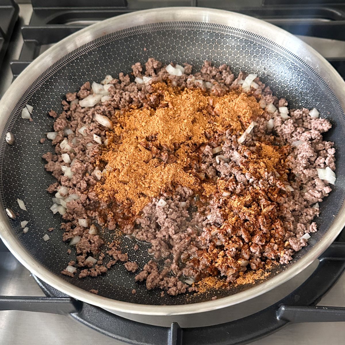 Skillet with ground beef, diced onions, and taco seasoning.