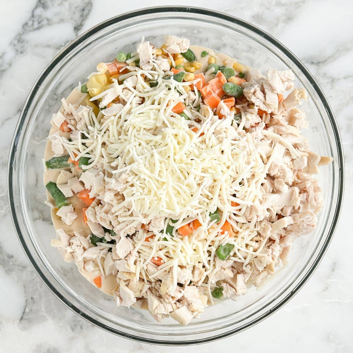 Bowl of shredded chicken, tortellini, alfredo sauce, vegetables, and shredded cheese. 