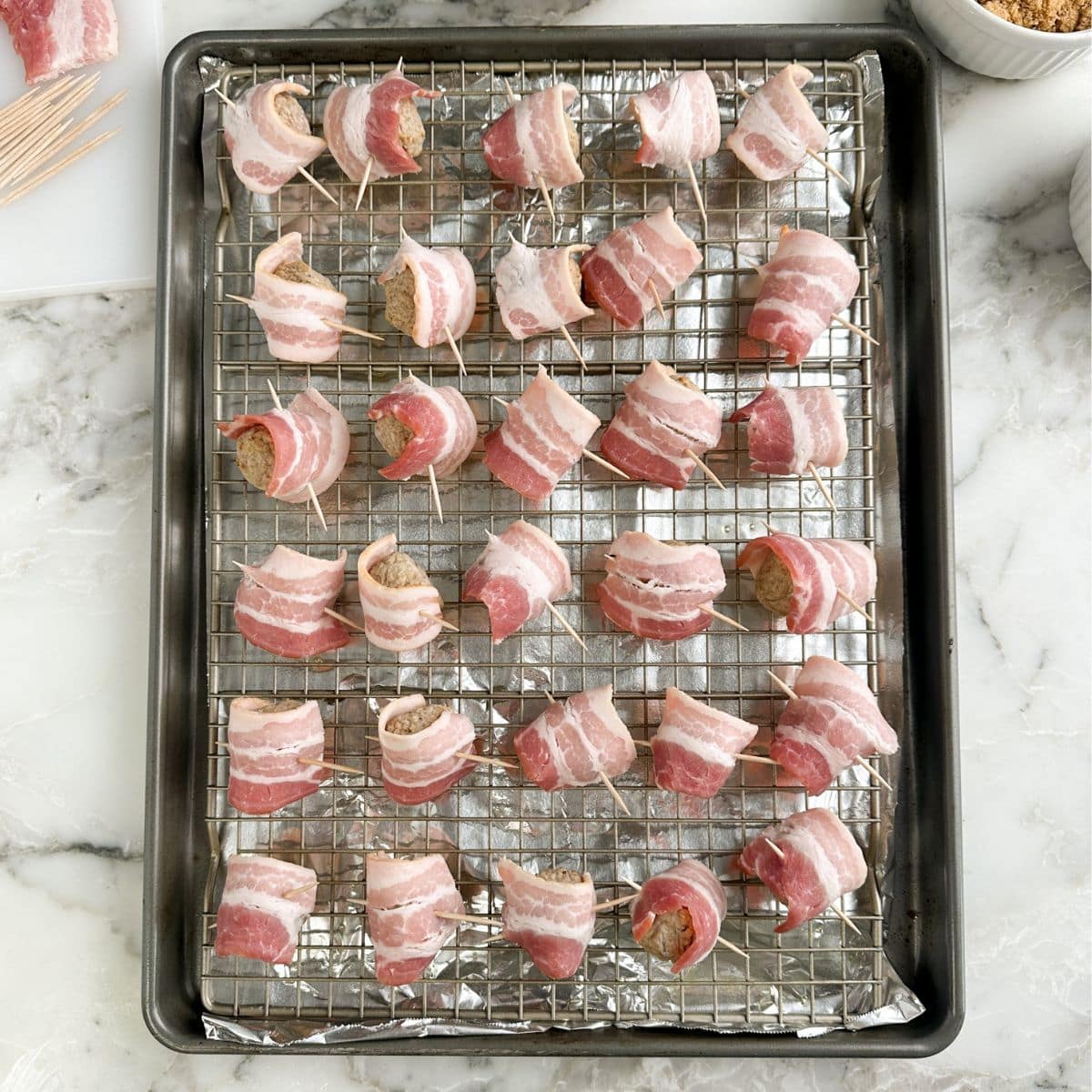 Baking dish with uncooked bacon wrapped meatballs. 
