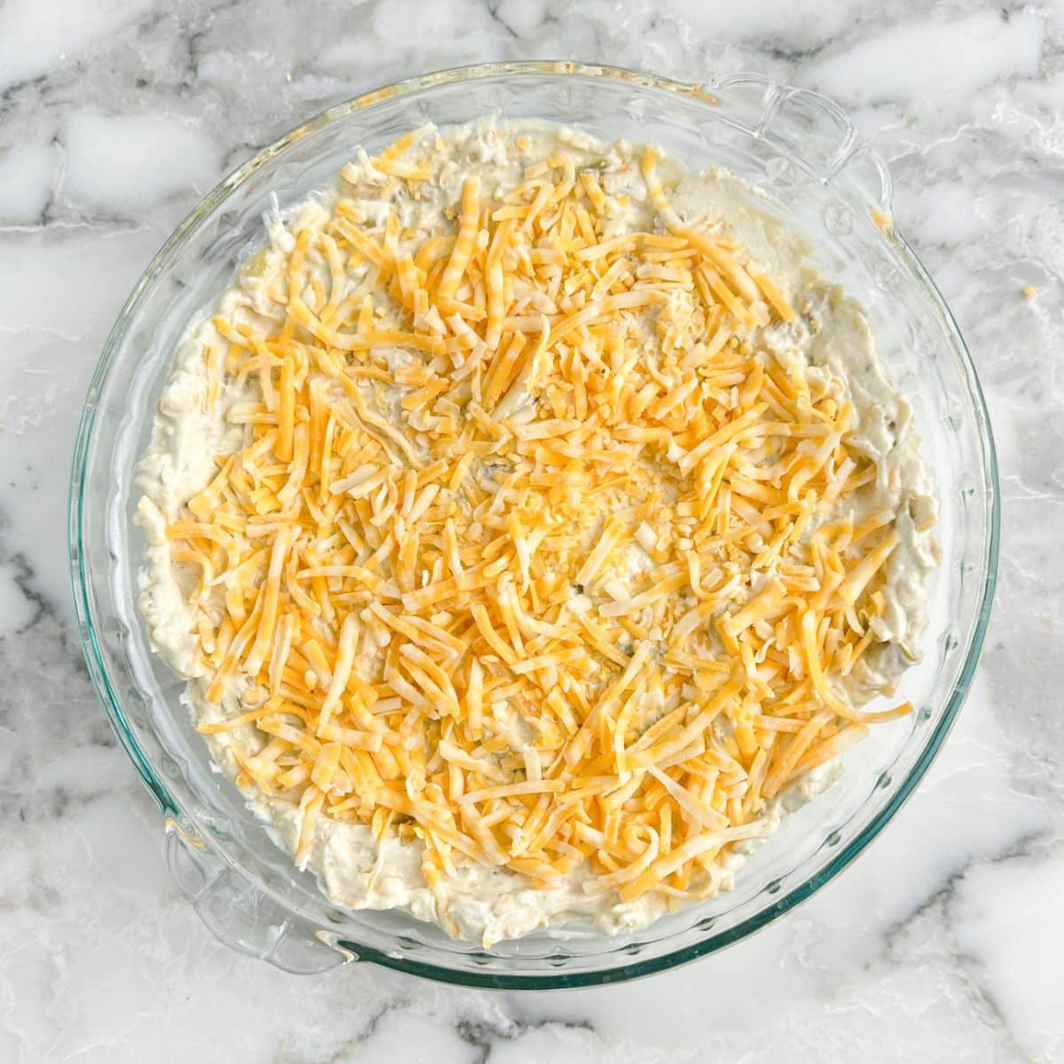 Pie dish with cream cheese dip topped with shredded cheese.