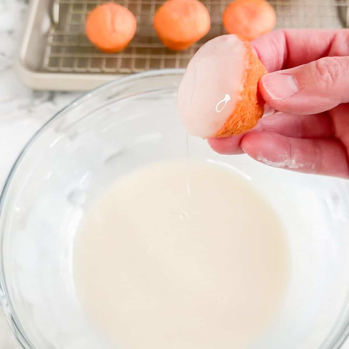 Bowl of icing with a mini strawberry cake dipping in the icing. 