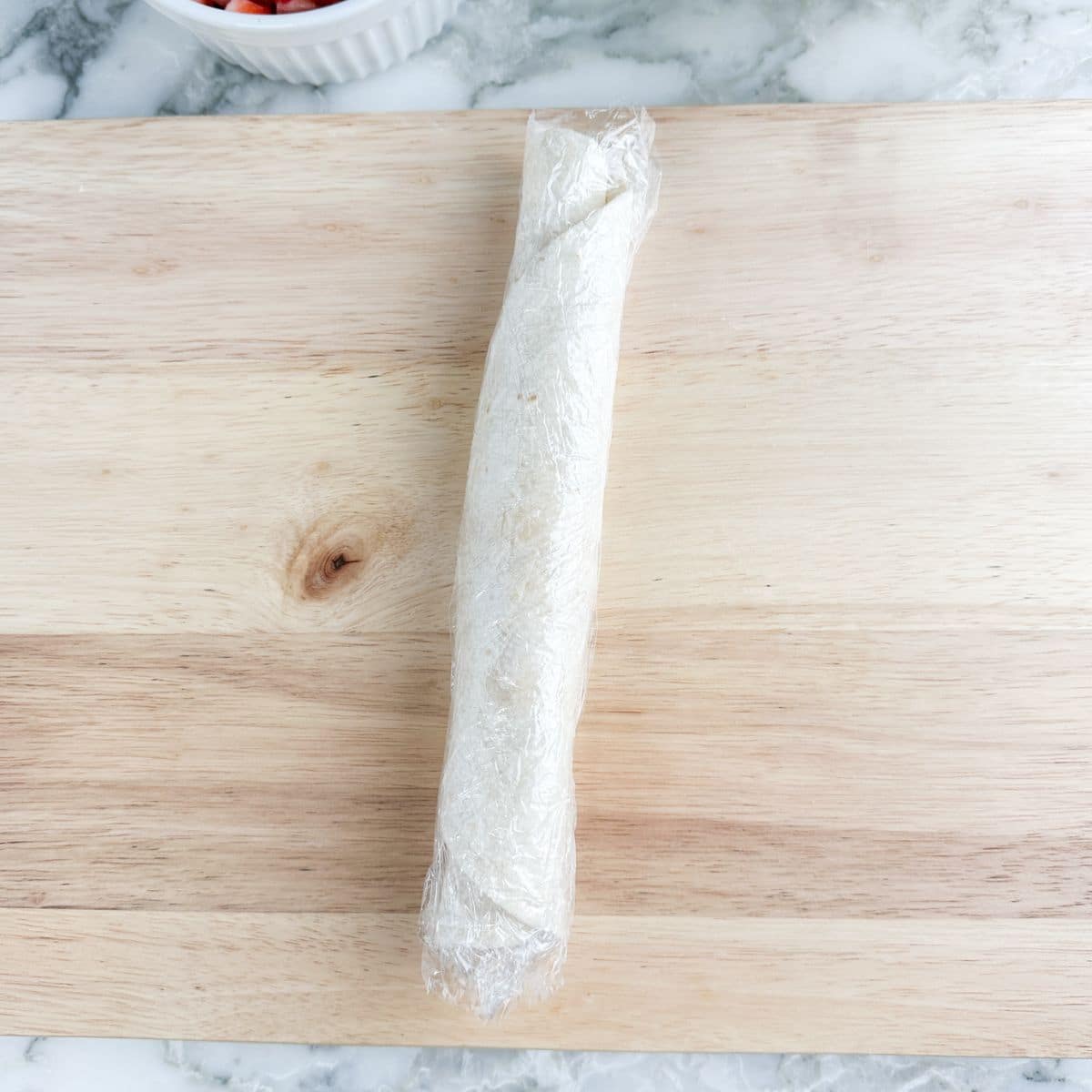 Rolled up tortilla wrapped in plastic wrap. 