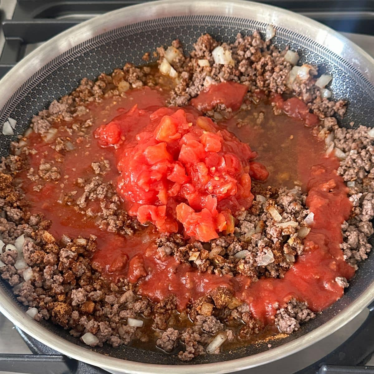 Skillet with ground beef, tomato sauce, and diced tomatoes.