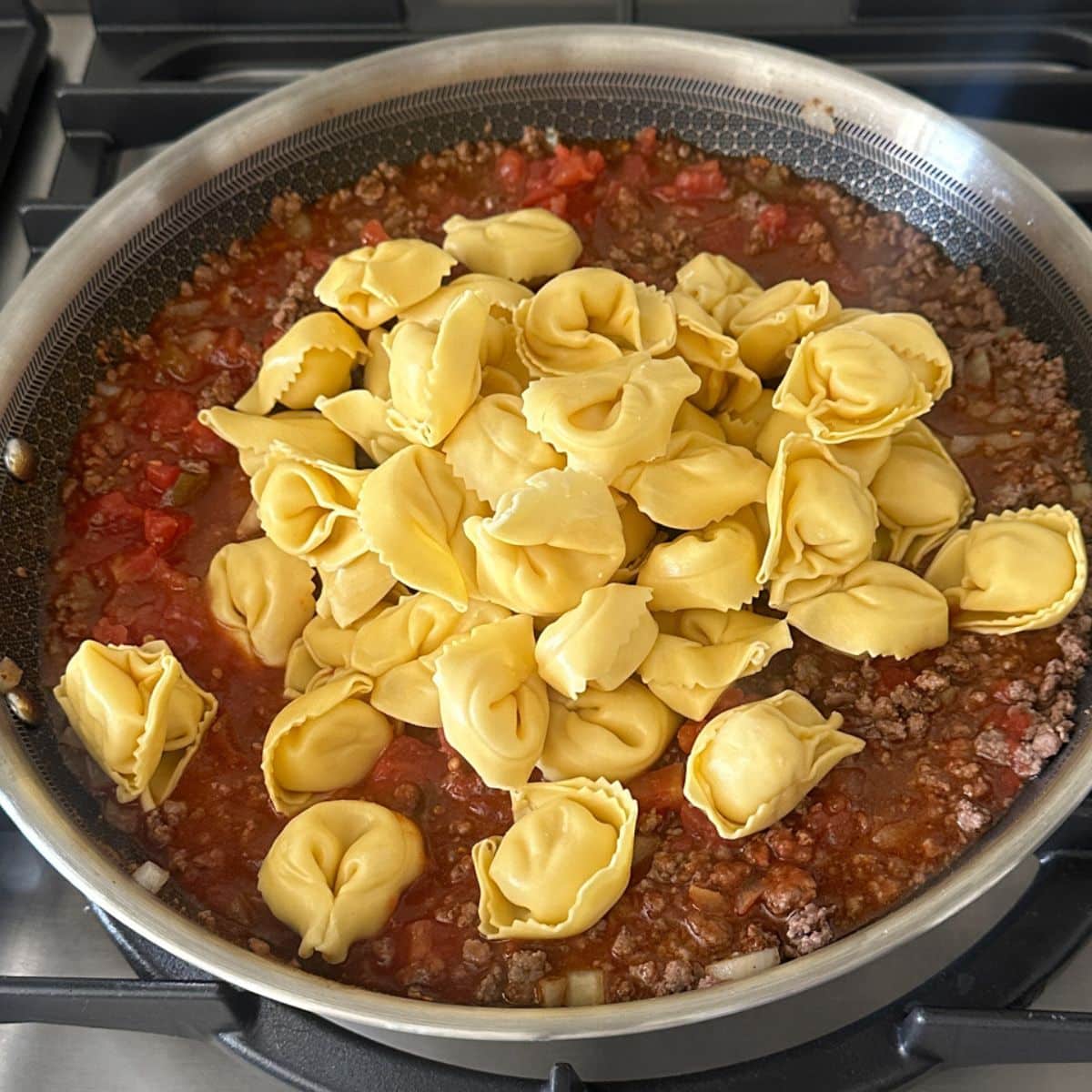 Skillet with ground beef, tomato sauce, and tortellini.