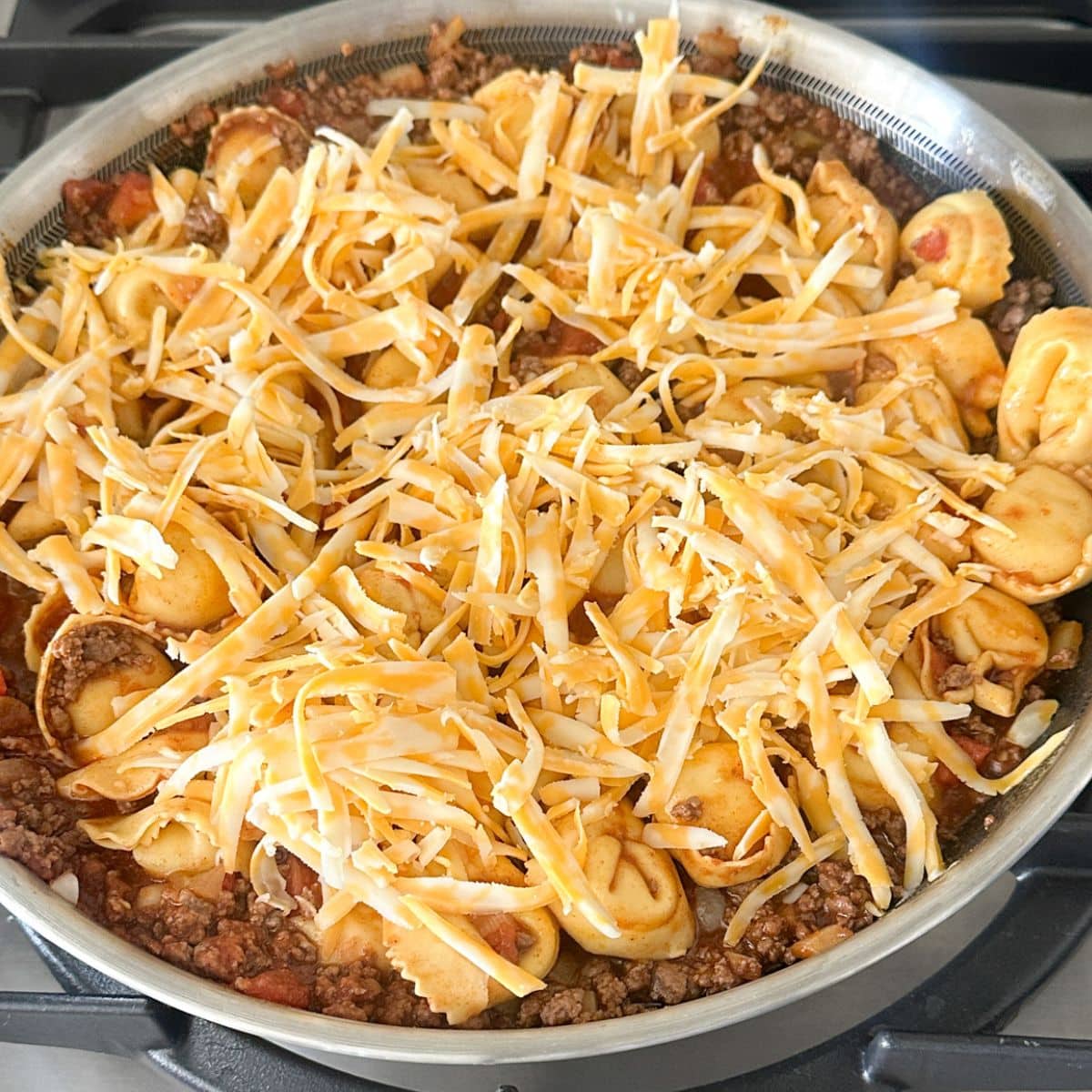 Skillet with taco tortellini topped with shredded cheese.