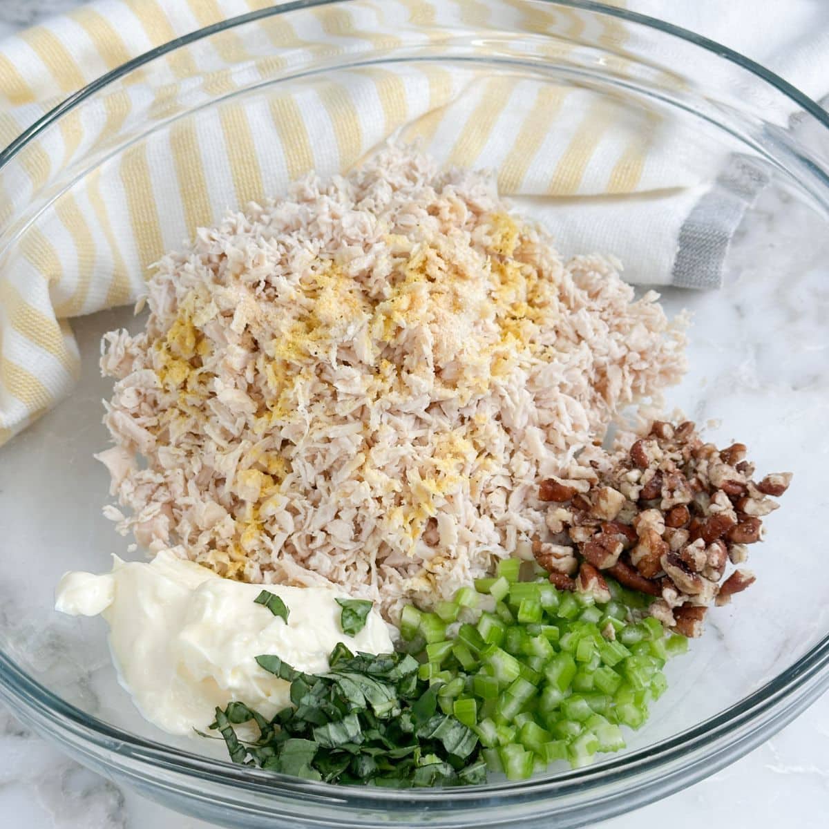 Bowl with shredded chicken, celery, mayonnaise, and chopped pecans.