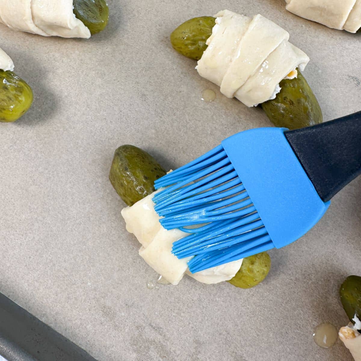 Butter being brushed on crescent roll pickles. 