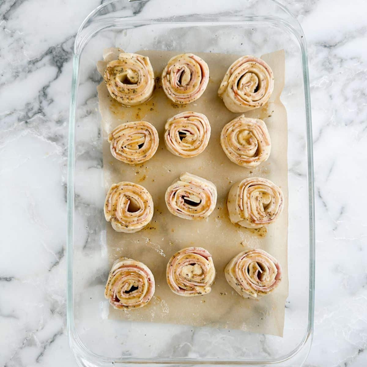 Baking dish with uncooked ham and cheese pinwheels. 