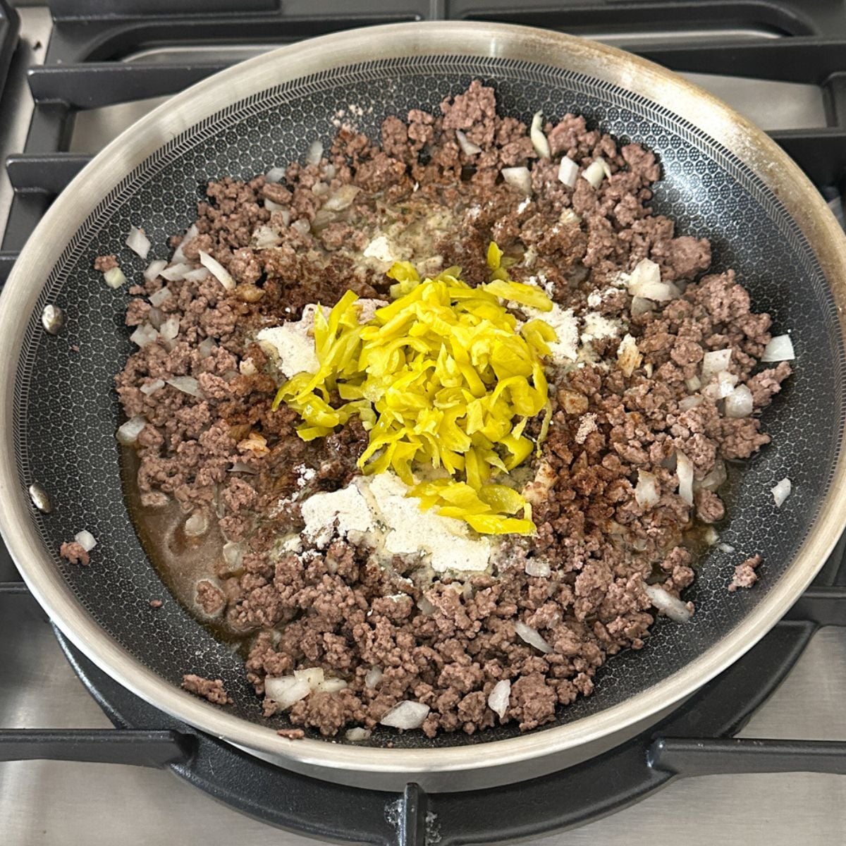 Skillet with ground beef, pepperoncinis, and seasonings. 