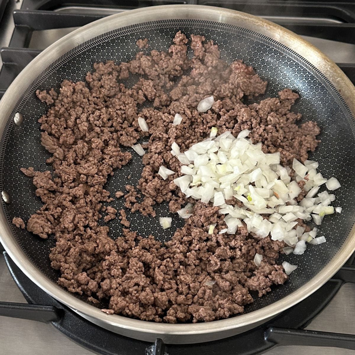 Skillet with ground beef and diced onions. 