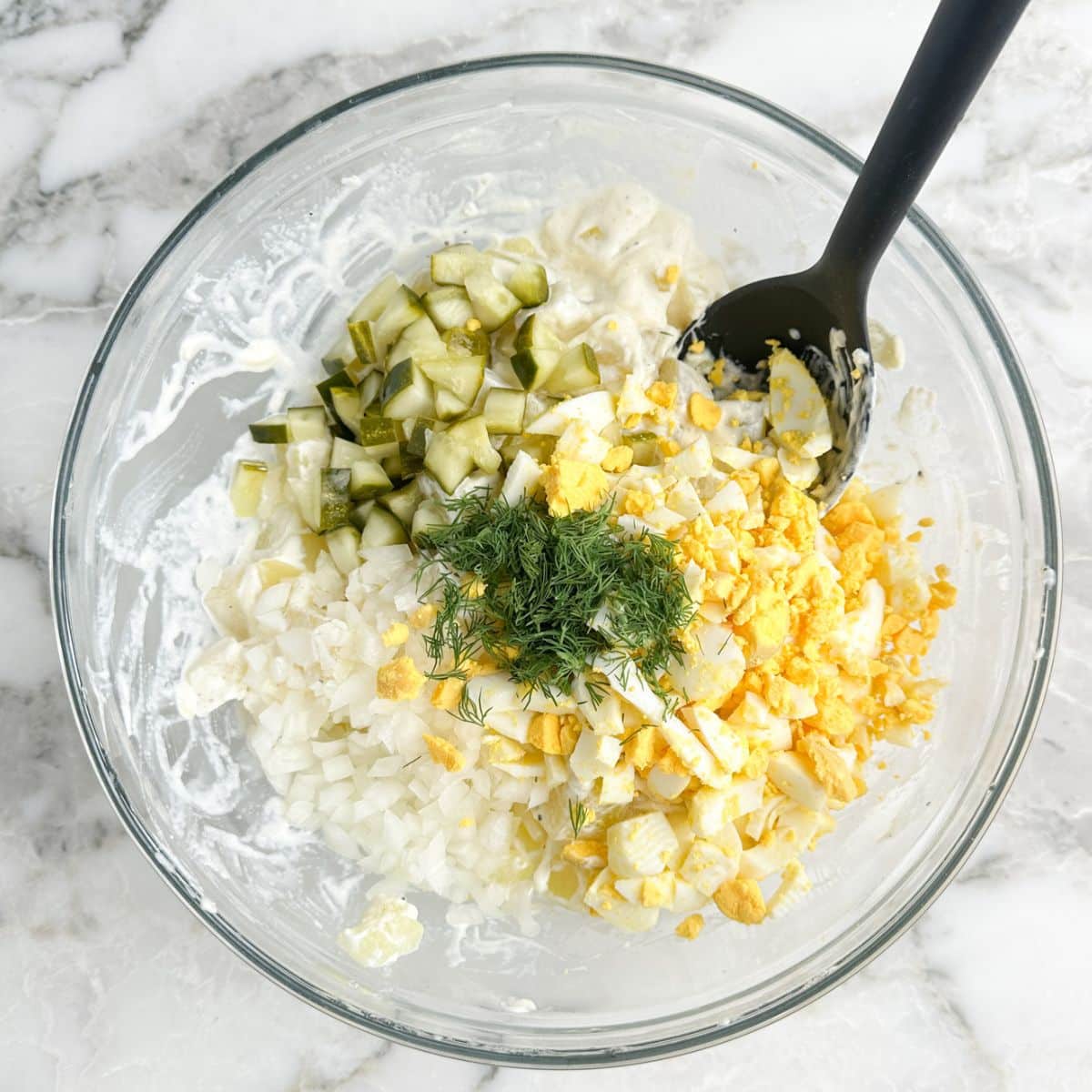 Bowl with diced potatoes, chopped eggs, pickles, and dill. 